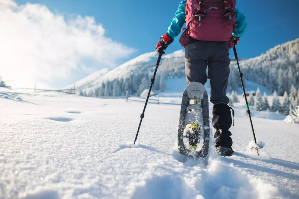Una donna con zaino e racchette da neve scala una montagna innevata