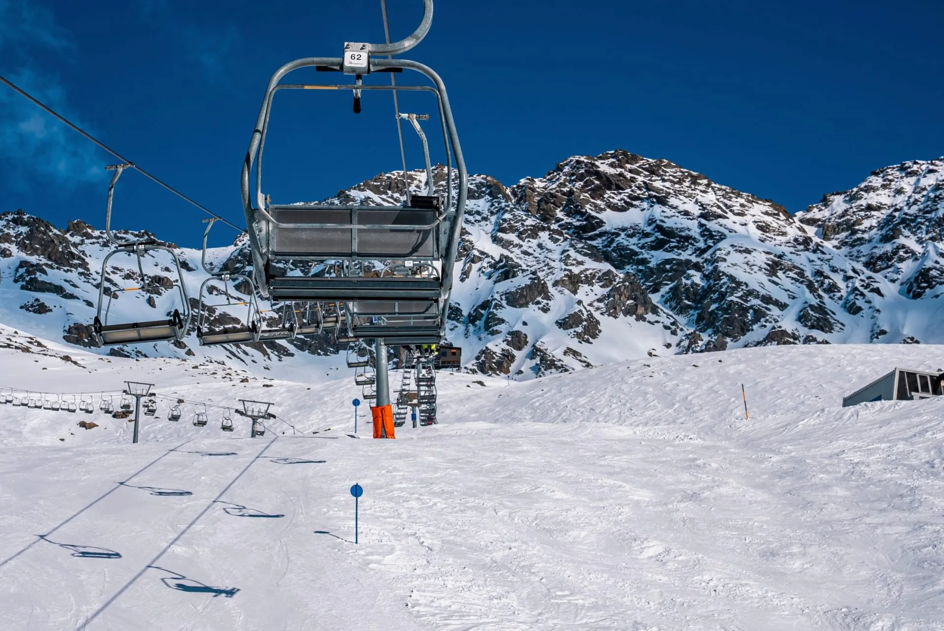 Empty chairlifts at ski resort against snowcapped mountains during sunny day