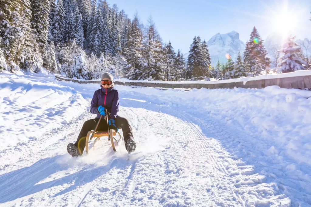 Chica alegre montando un trineo cuesta abajo, nieve, paisaje soleado de invierno