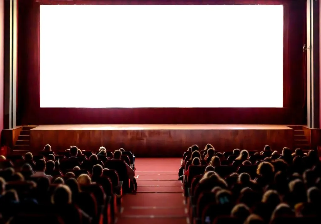 Ihmisiä elokuvateatterin salissa, jossa on tyhjä valkoinen valkokangas.