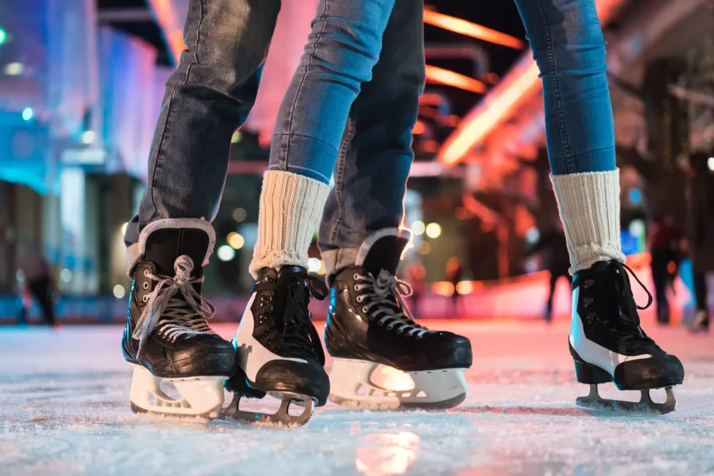 primer plano parcial de joven pareja en patines patinando sobre hielo en pista