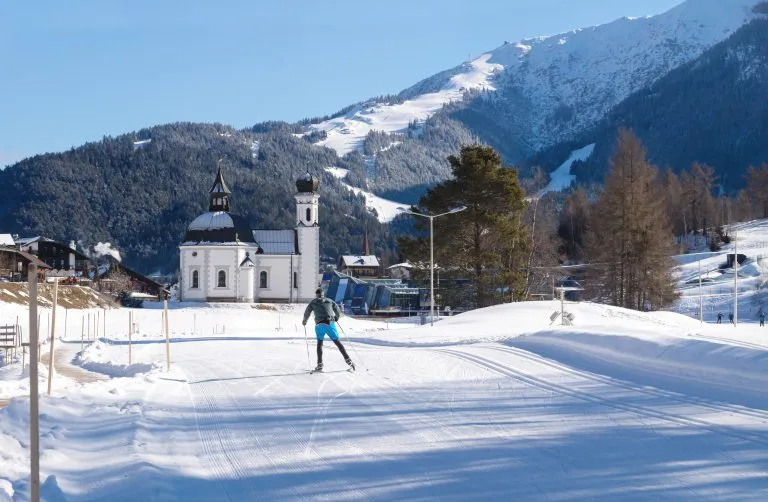 Sciatore di fondo su una pista soleggiata verso una chiesa pitoresca, Seefeld, Austria