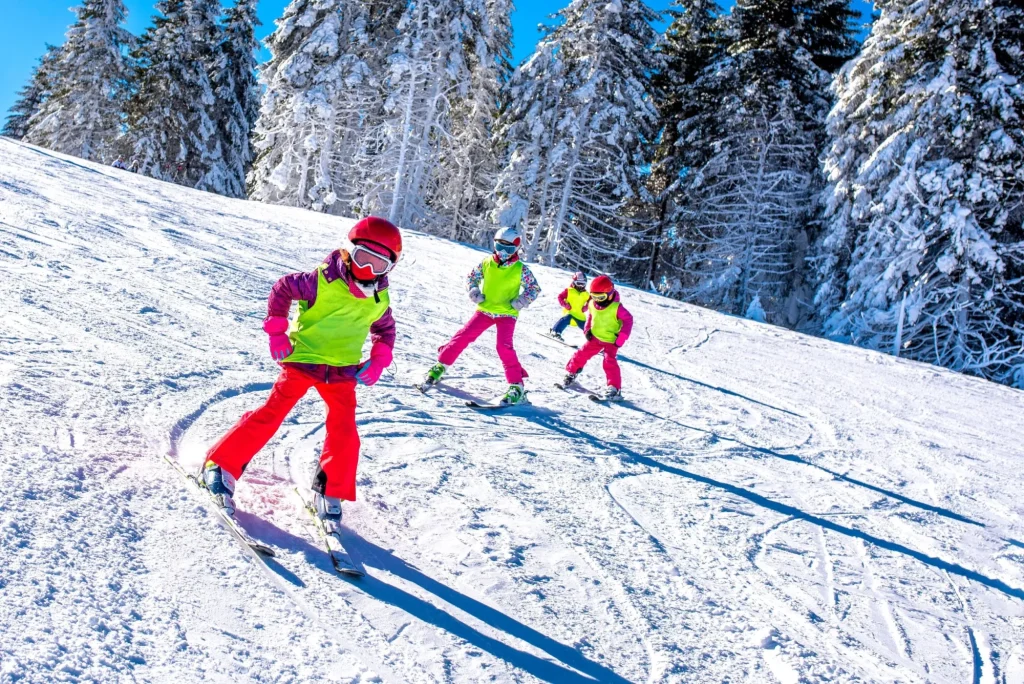 Grupp av barn som lär sig åka skidor på sluttning i berg under vintersemester
