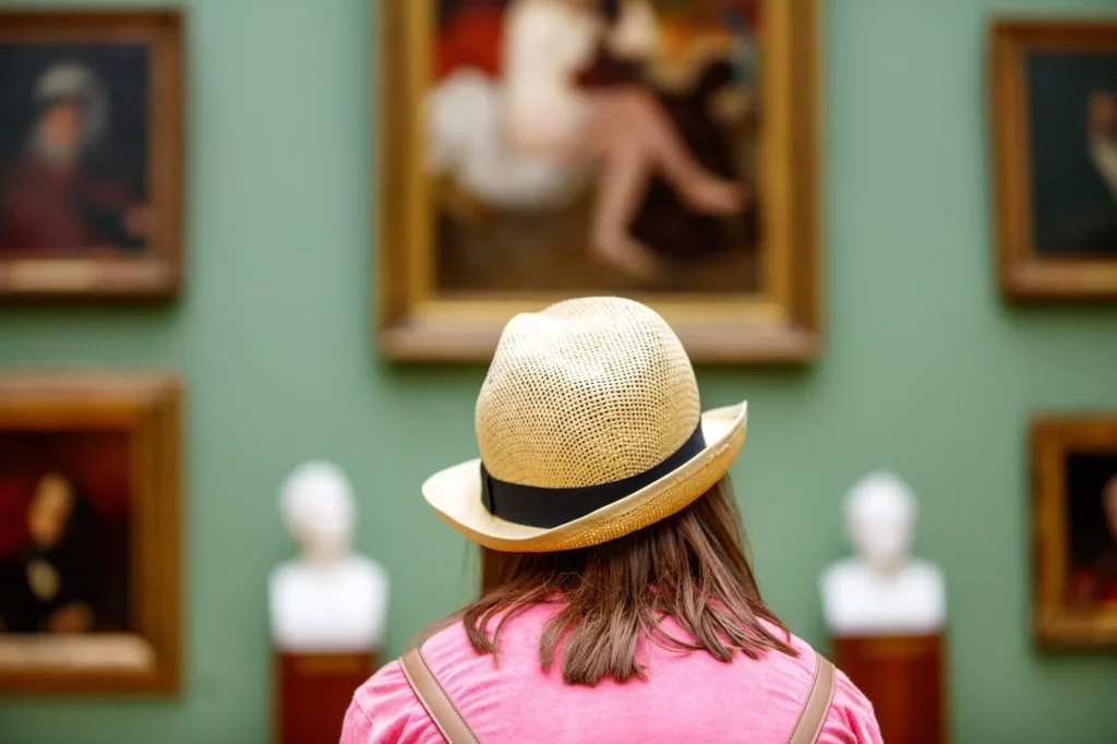 Flicka i hatt tittar på målningar på ett museum