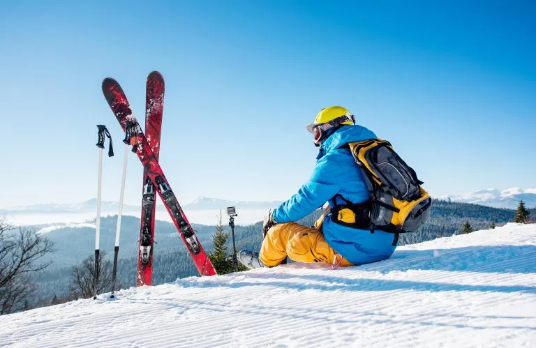 Vue arrière d'un skieur assis au sommet de la montagne près de son équipement de ski, se relaxant et profitant de belles montagnes enneigées, vue sur des personnes vivant des plaisirs récréatifs, voyageant à cheval.
