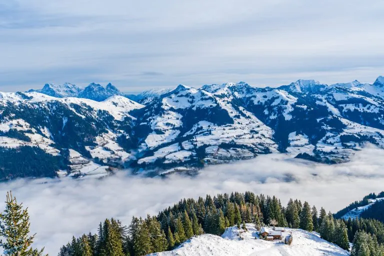 Panoramaflyfoto av vinterlandskap i de østerrikske Alpene over lave skyer som dekker Kitzbühel i Østerrike.