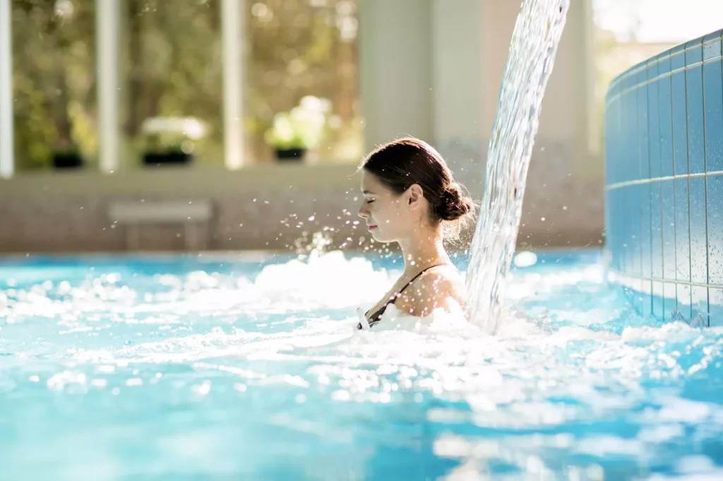 Jeune fille sereine profitant d'une chute d'eau et de ses doux éclaboussures dans la piscine d'une station thermale.