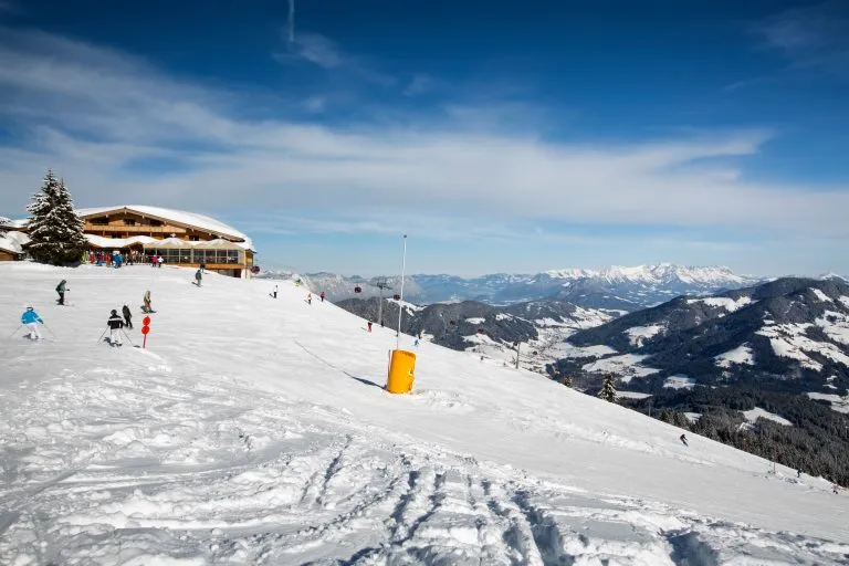 Panoramautsikt over skibakke på solrik vinterdag i alpinanlegg. Folk står på ski ned bakken.