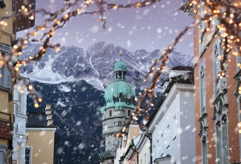 Tetti di Innsbruck con montagne sullo sfondo e luci di Natale in primo piano in una serata invernale di neve