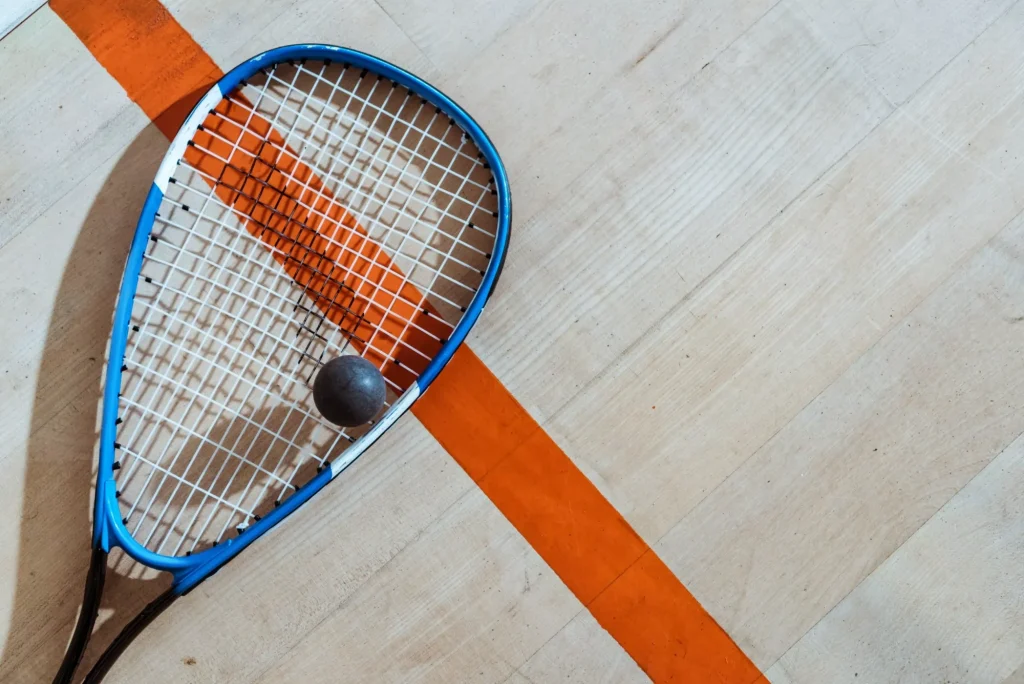 Vista superior de raqueta de squash y pelota sobre superficie de madera