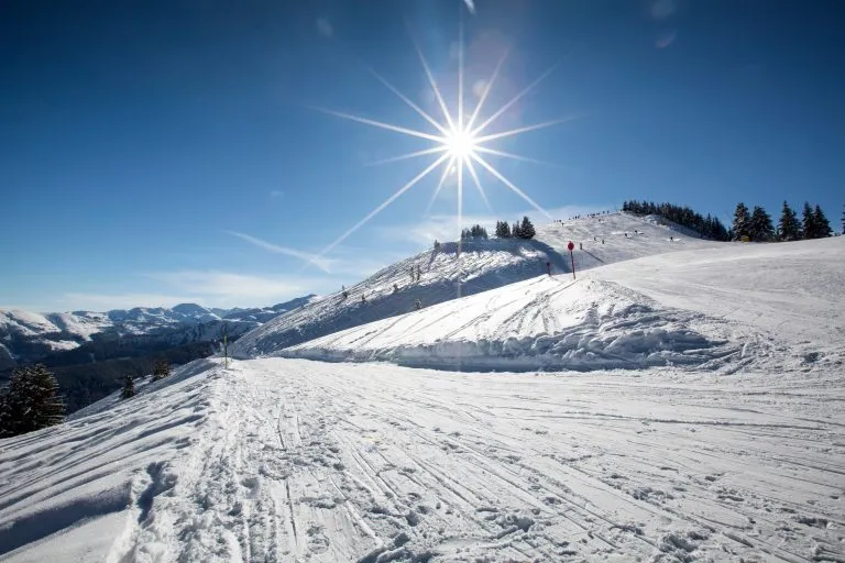 Panoramiczny widok na stok narciarski w zimowy słoneczny dzień w alpejskim ośrodku narciarskim. Ludzie zjeżdżający na nartach.