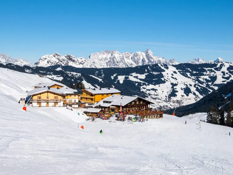 Laskettelurinne ja apres ski -vuoristomökki, jossa on ravintolan terassi Saalbach Hinterglemm Leogangin talviurheilukeskuksessa, Tirol, Itävalta, Eurooppa. Kuvattu aurinkoisena päivänä.