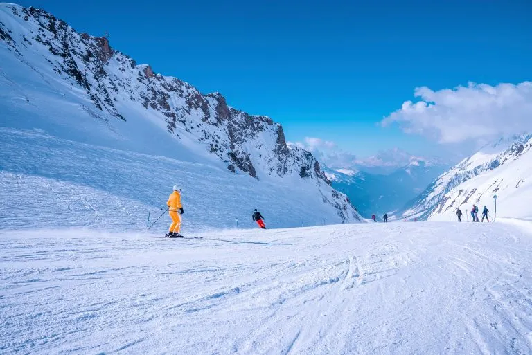 St. Anton am Arlberg. 10 mars 2022. Människor i skidkläder glider nedför backen på snöigt berg på skidort under vacker solig dag, Skidåkare skidar nedför på snöigt berg