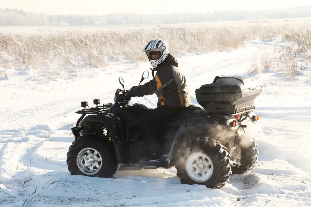 mężczyzna prowadzący quada na zimowym polu