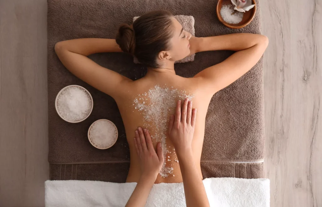 Jeune femme effectuant un gommage du corps au sel de mer dans un salon de spa, vue de dessus